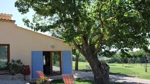 A house with a patio area, two chairs, and a tree providing shade.
