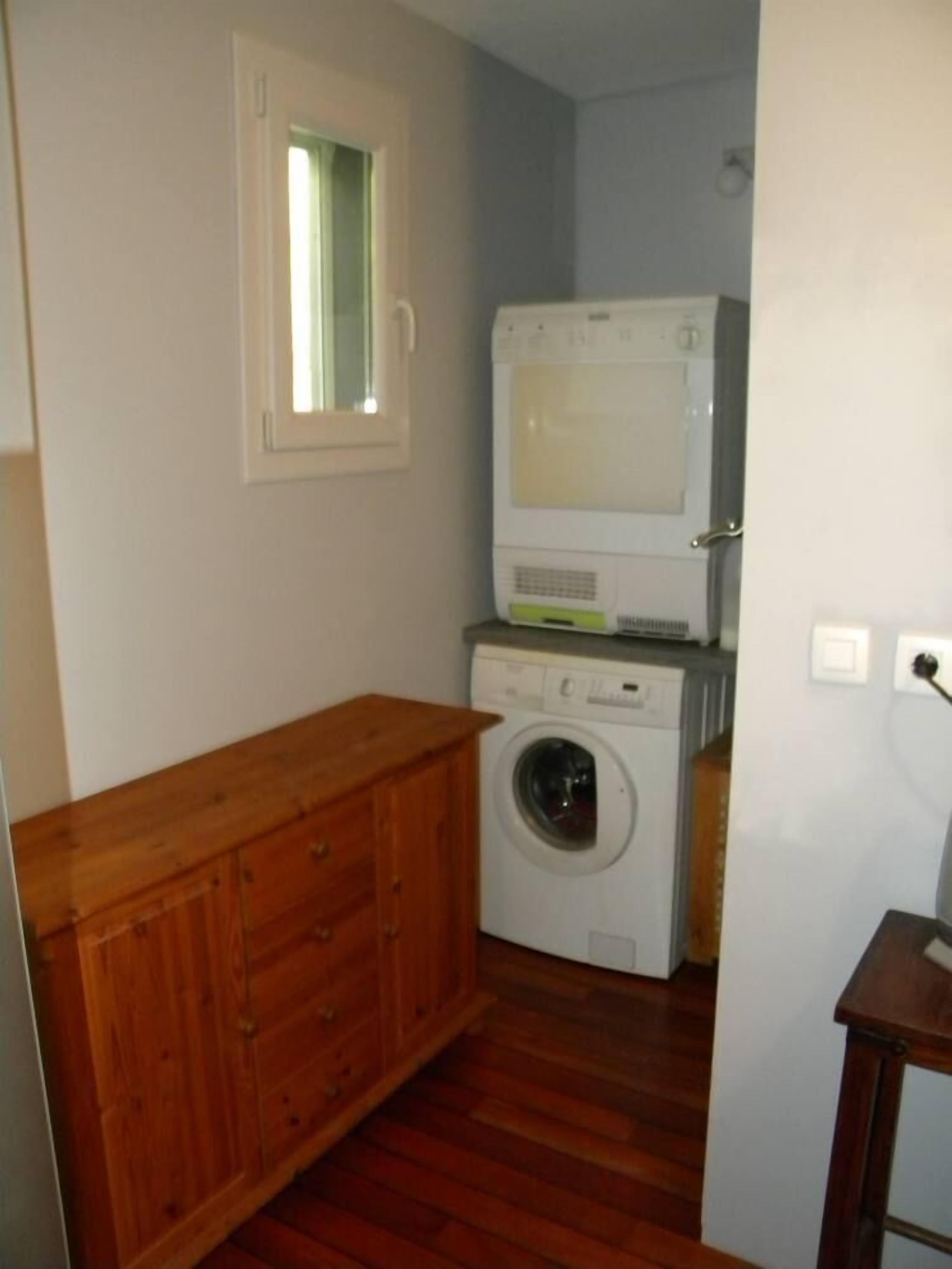 Une buanderie équipée d’un lave-linge et d’un sèche-linge, de placards en bois et d’une fenêtre.
