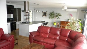 Un salon avec un canapé en cuir rouge, une table basse en bois et une cuisine en arrière-plan.