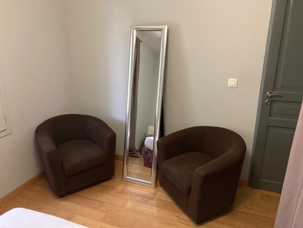 A room with two brown armchairs, a tall mirror, a wooden floor, and a green door.