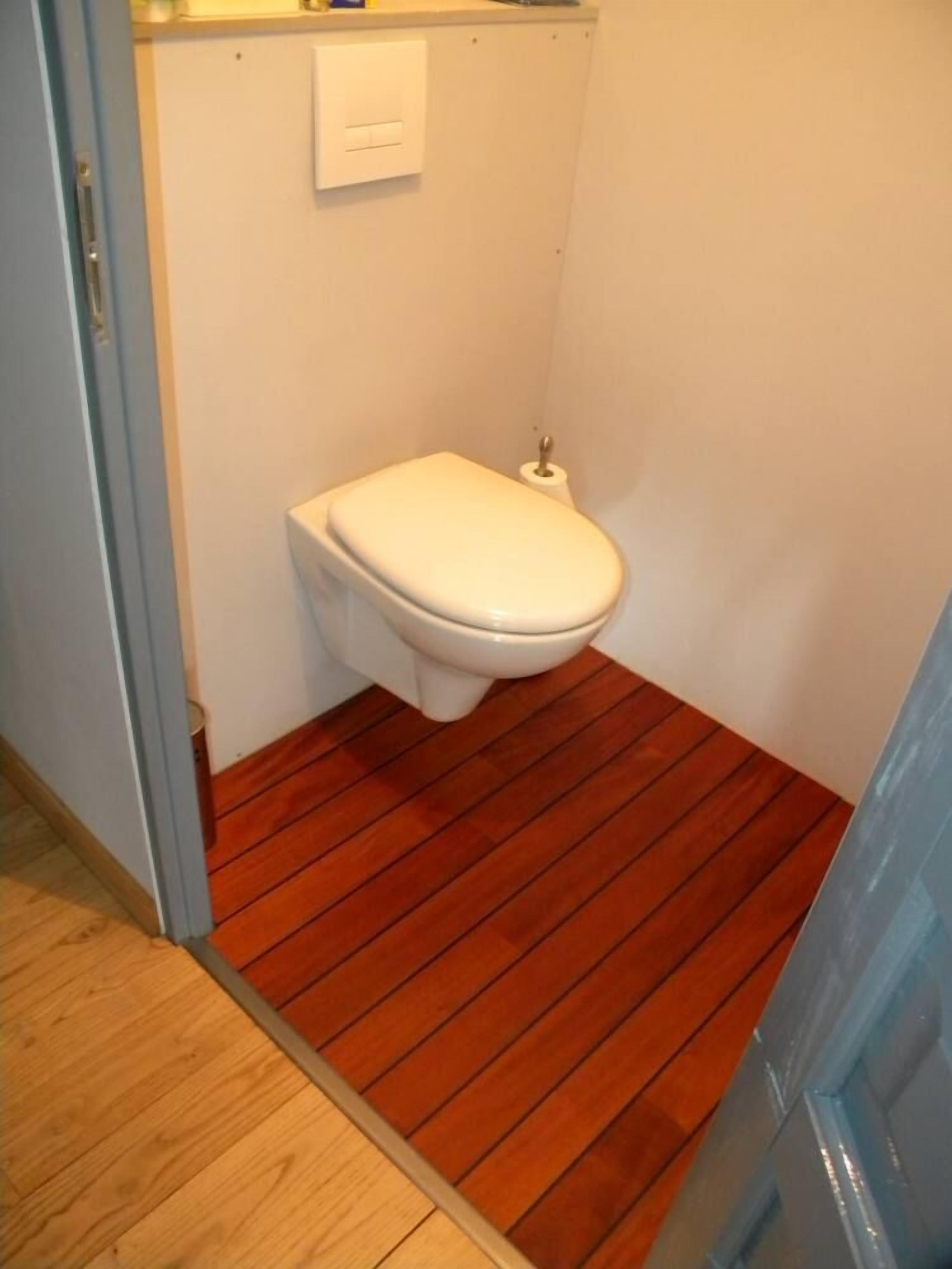A small bathroom with a white toilet, wooden flooring, and a white wall.