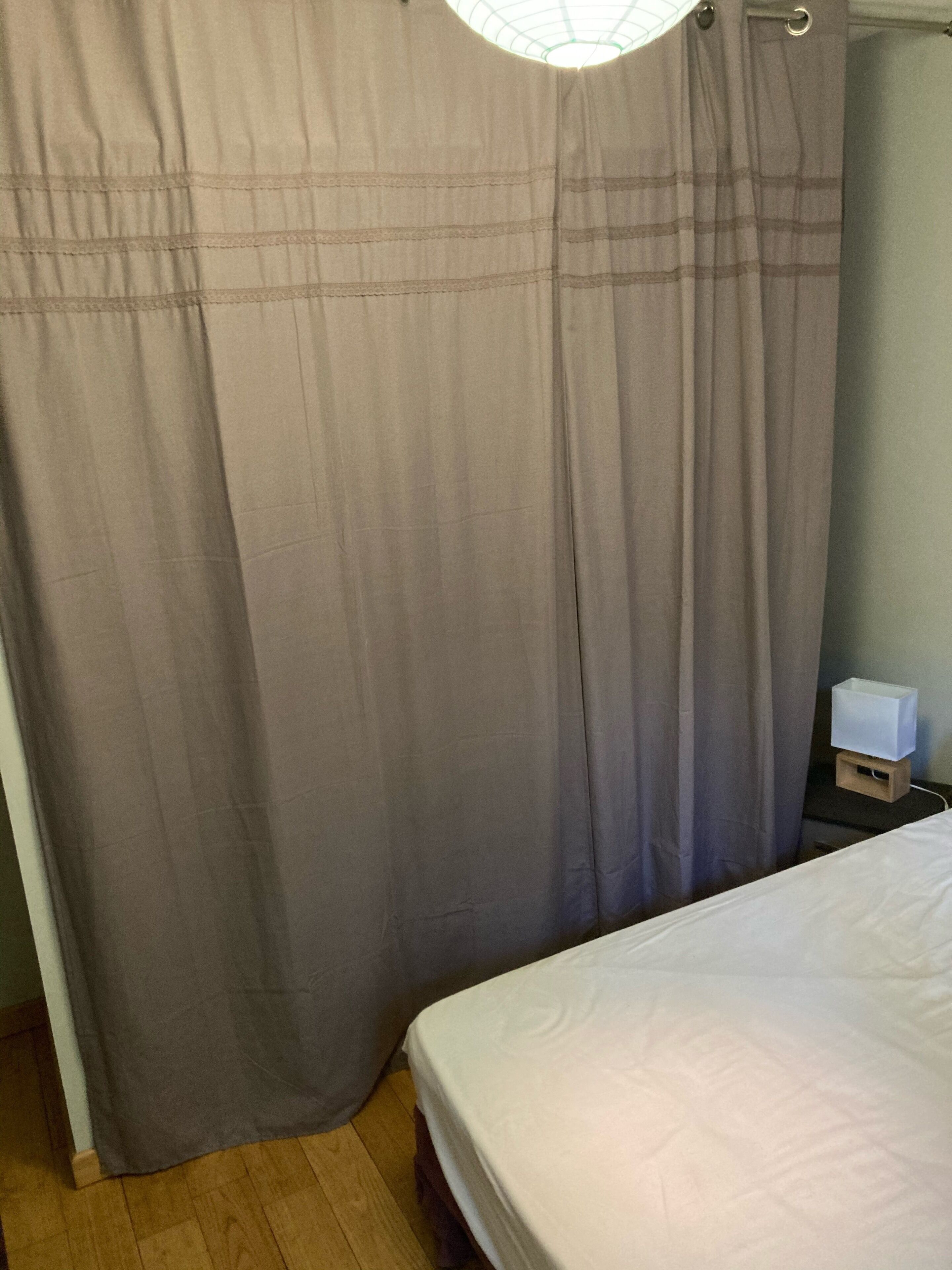 A bedroom with a bed, a nightstand with a lamp, and a window with curtains.