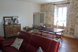 Un salon avec un canapé en cuir rouge, un meuble en bois et une table à manger avec des chaises. Il y a un mur en pierre et une fenêtre avec vue.