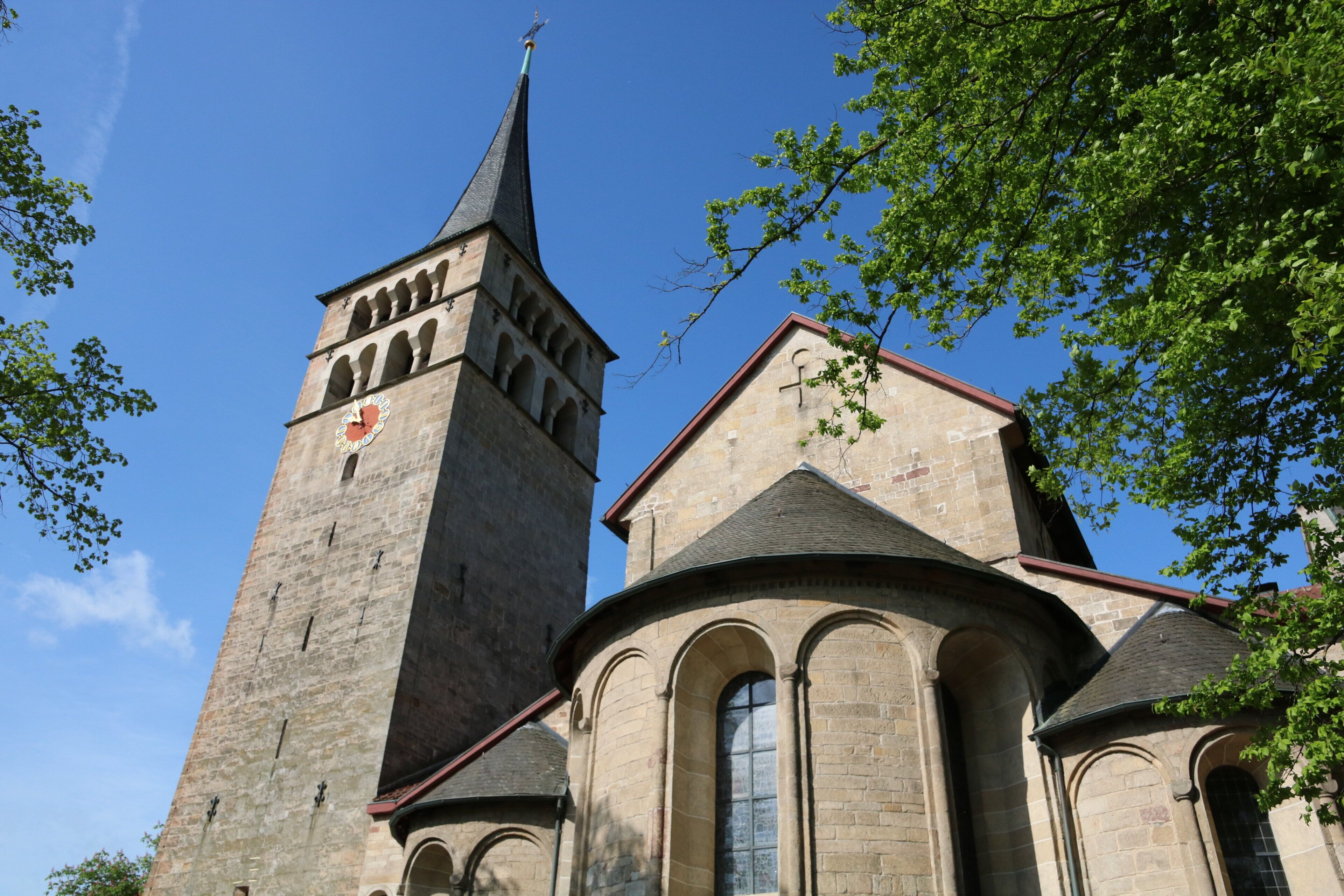 A church with a tall tower and a smaller adjacent building, both featuring arched windows and stone construction.