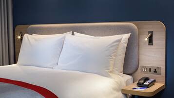 A hotel room with a bed, a bedside table with a phone, and a power outlet.
