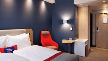 Una habitación de hotel con una cama, una silla roja, una mesita y una puerta.
