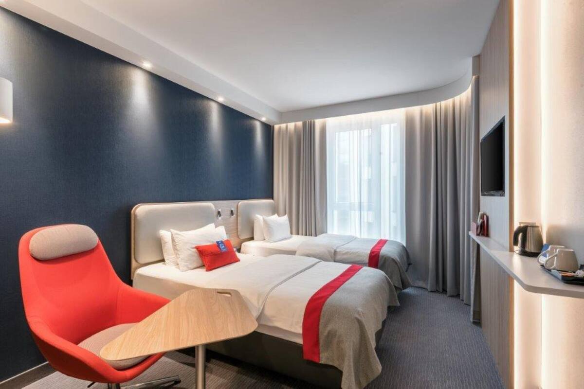 A hotel room with two beds, a red armchair, a bedside table, and a TV.