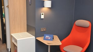 A modern room with a wooden desk, a red chair, a small table with a sign, and a wall-mounted light fixture. - Holiday Inn Express Sindelfingen by IHG (Sindelfingen)