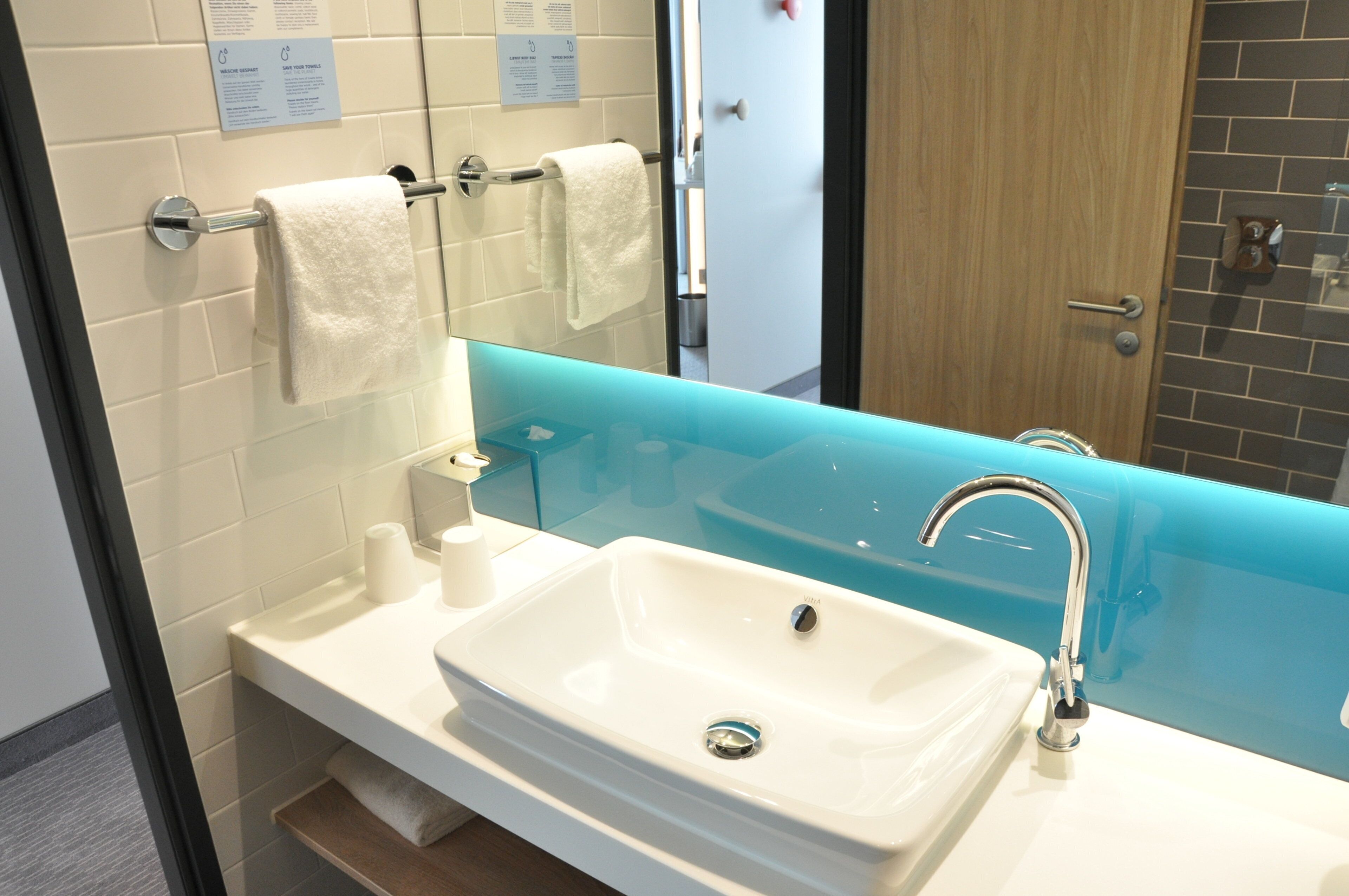 A bathroom with a white sink, a glass partition, and a mirror.