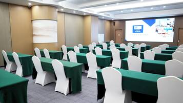 A conference room with rows of tables and chairs, a projector screen, and a presentation slide.
