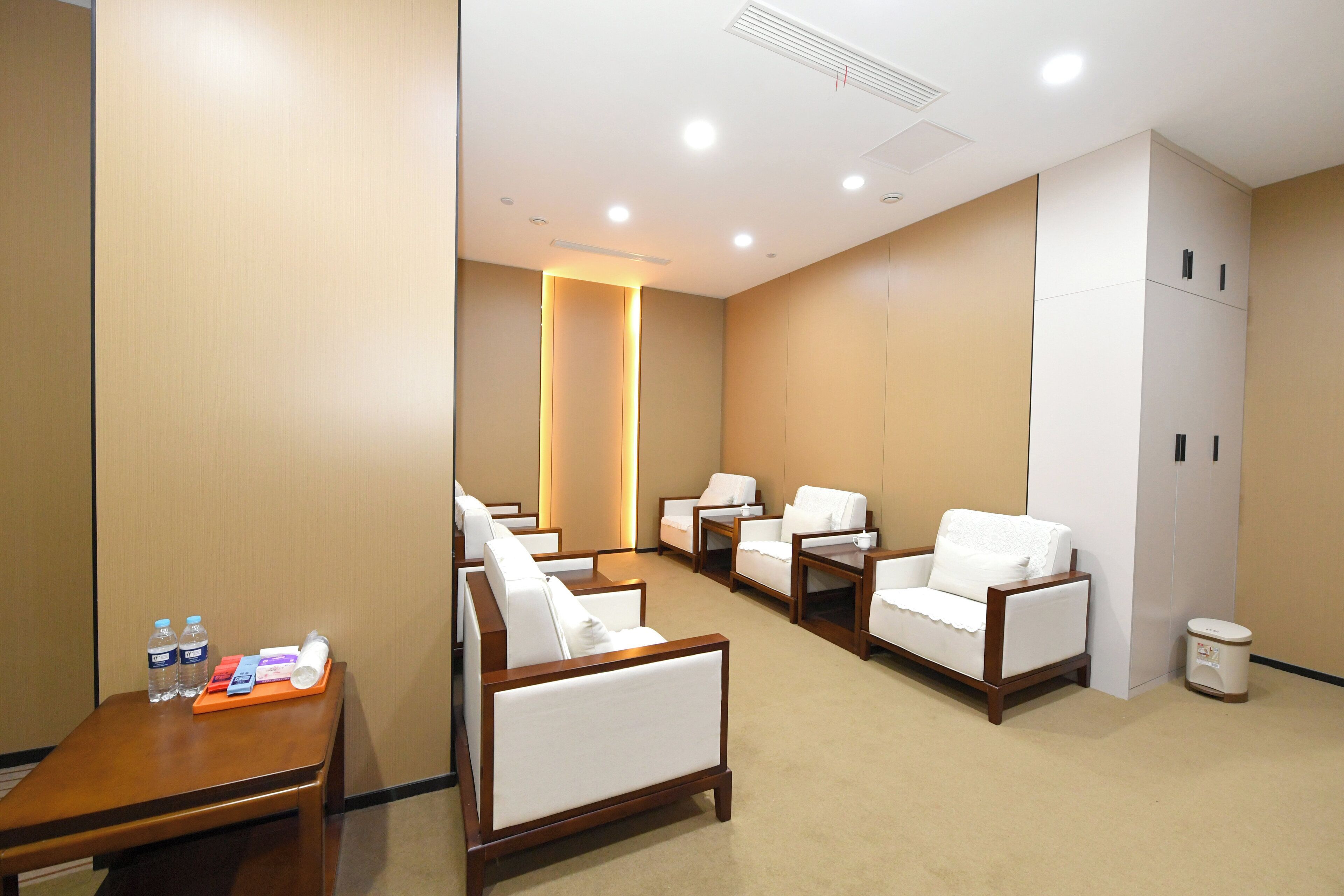 A hotel room with a seating area, a small table with a tray of items, and a trash bin.