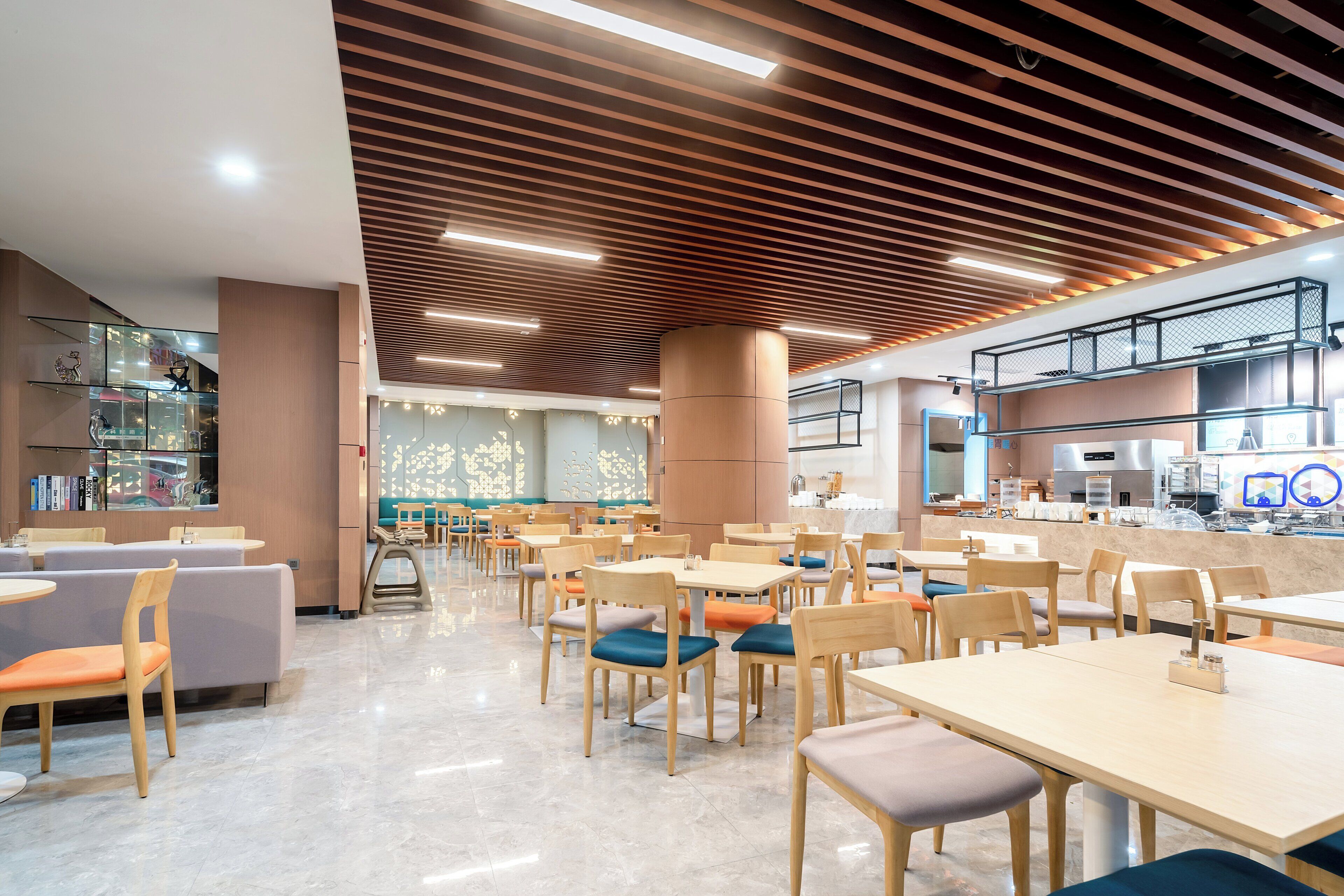 A modern cafe with wooden tables and chairs, a kitchen area, and a seating area with a view.