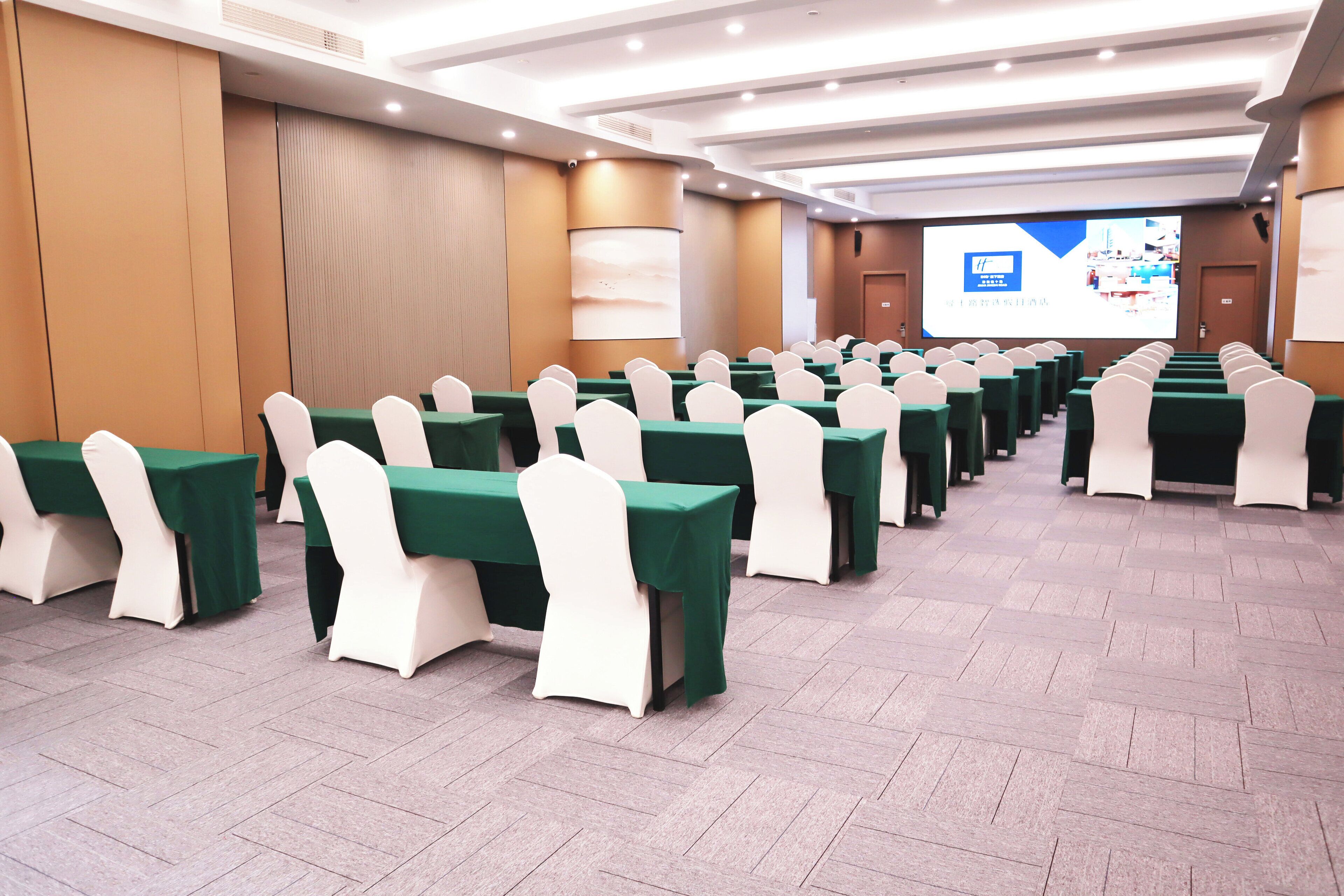 A conference room with rows of tables and chairs, a projection screen, and a presentation area.