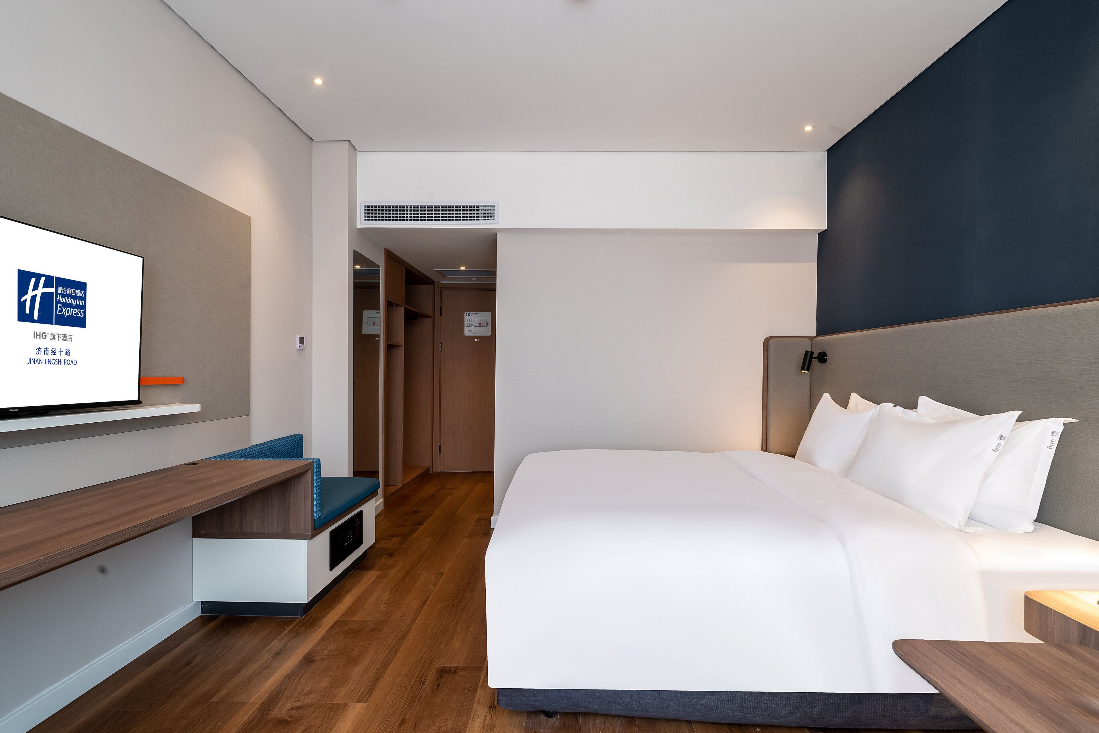 A modern hotel room with a large bed, a TV mounted on the wall, and a wooden bench.