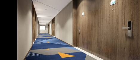 A long, narrow hotel corridor with a geometric patterned carpet, wooden panel walls, and a door with a number sign.