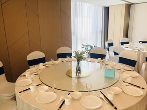 A round dining table with white tableware and chairs with blue sashes, set for a meal. - Holiday Inn Express Linyi North New District by IHG (Linyi)