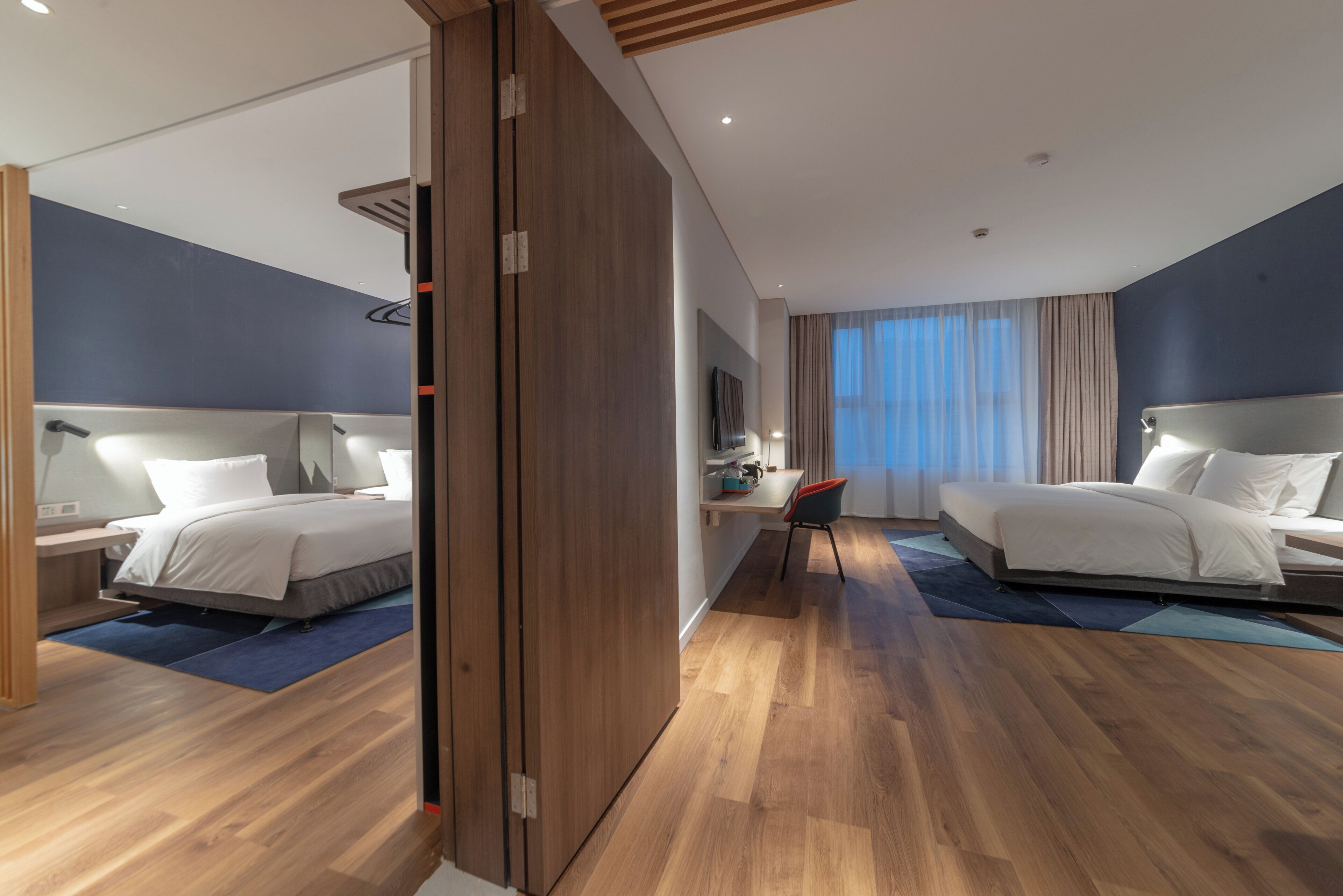 A hotel room with two beds, a desk, a chair, and a large mirror.