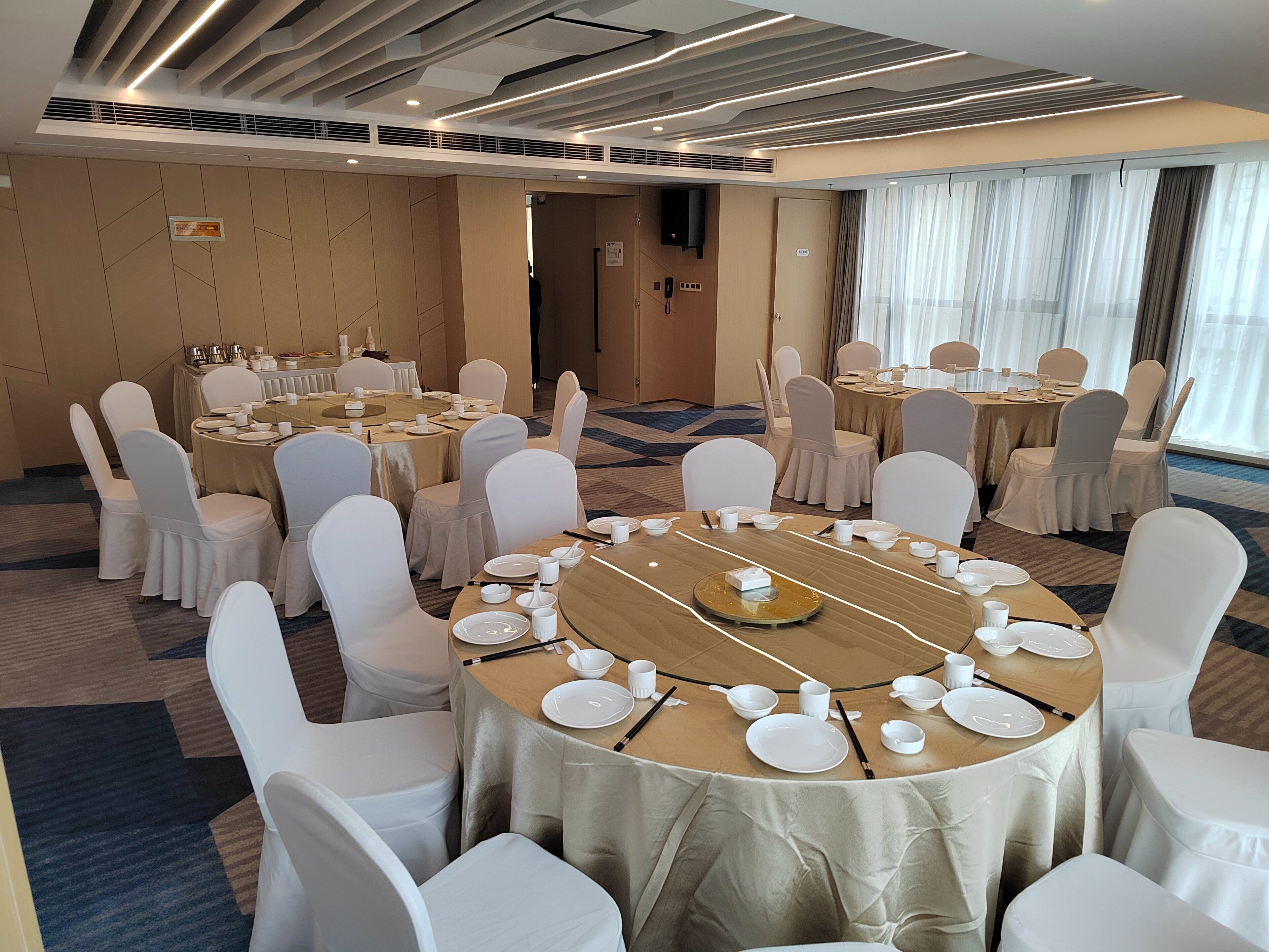 A conference room with round tables, white chairs, and a modern ceiling design.