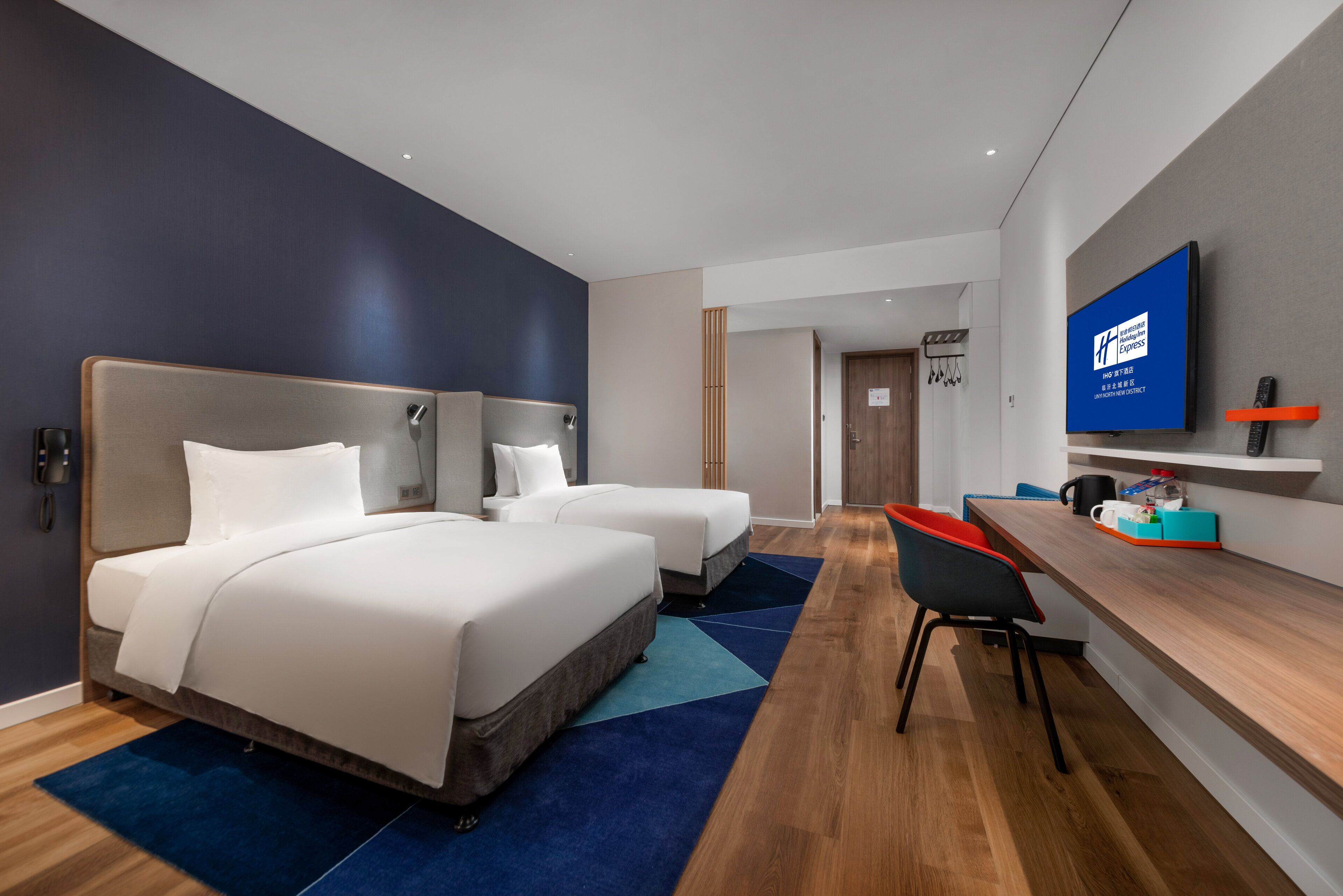 A modern hotel room with two beds, a desk, and a TV.
