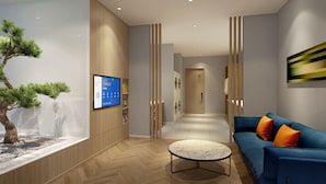 A modern living room with a blue sofa, a round coffee table, and a wall-mounted TV displaying a QR code. - Holiday Inn Express Linyi North New District by IHG (Linyi)