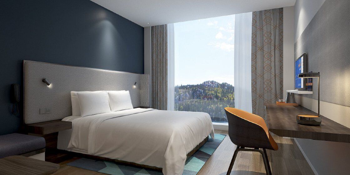 Quarto de hotel moderno com uma cama grande, uma escrivaninha e vista para o exterior.