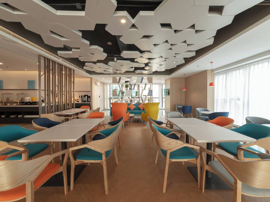 Un comedor moderno con paneles hexagonales en el techo, mesas de madera y sillas coloridas.
