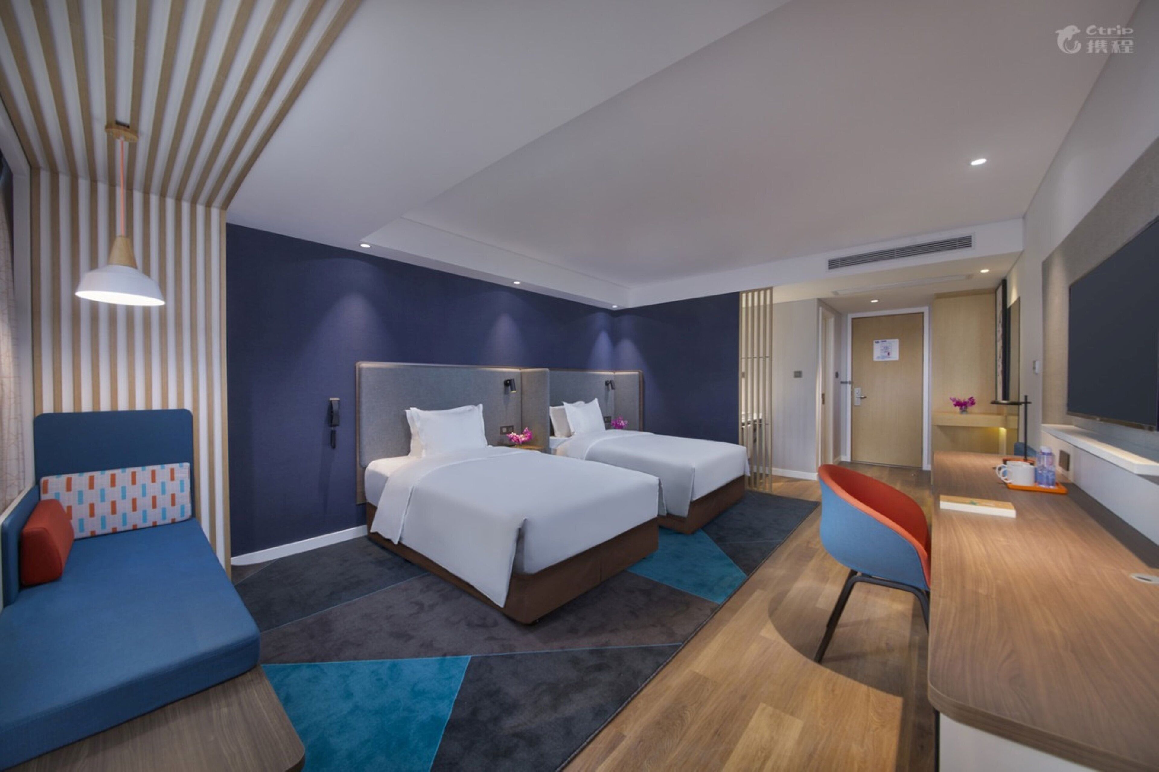 A modern hotel room with two beds, a sofa, a desk, and a TV.
