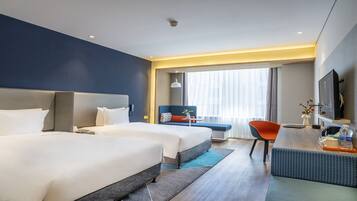 Una habitación de hotel con dos camas, un escritorio con silla, televisor y ventana con cortinas.