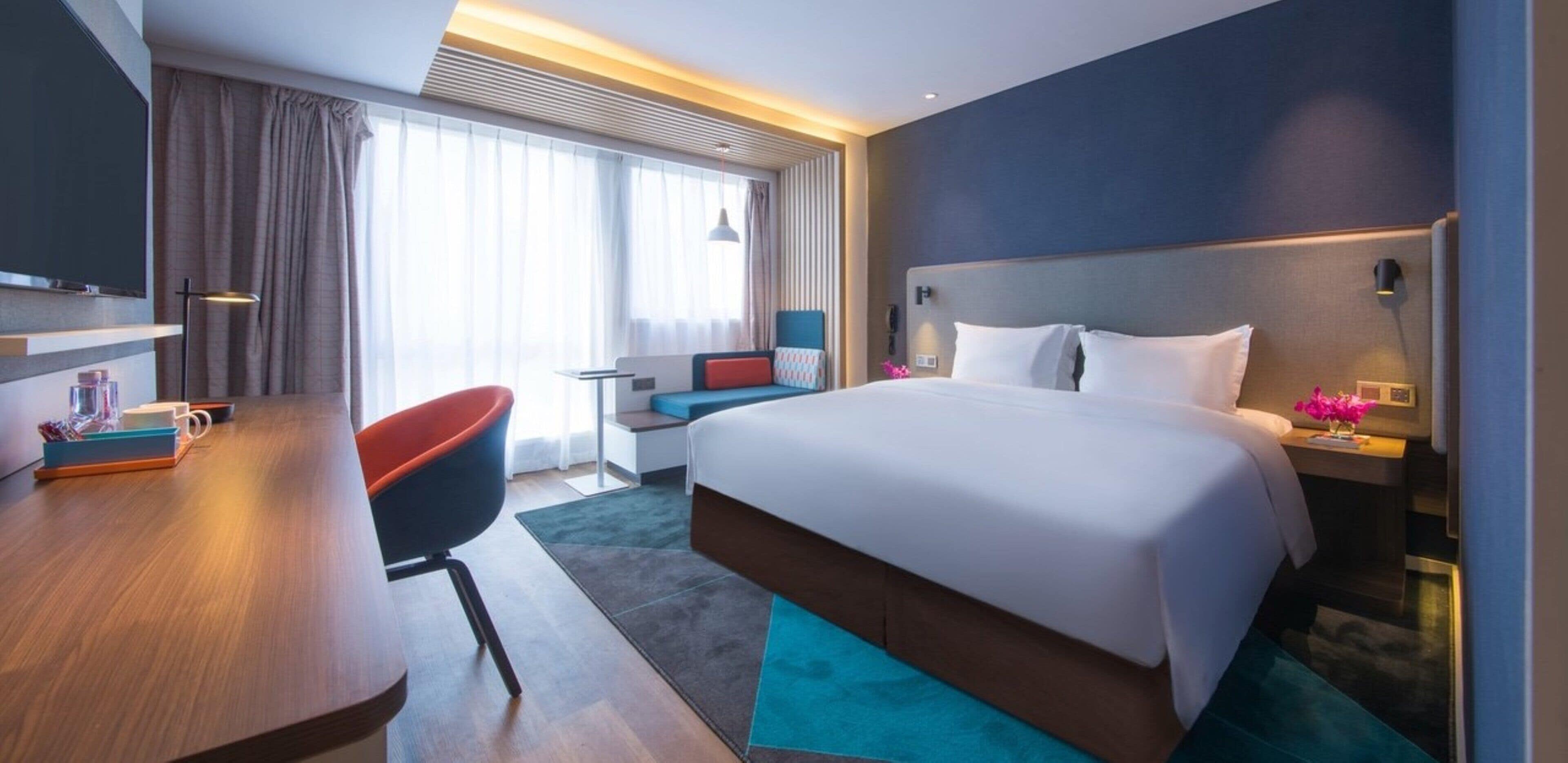 Habitación de hotel con una cama grande, un escritorio, una silla y una ventana con cortinas.
