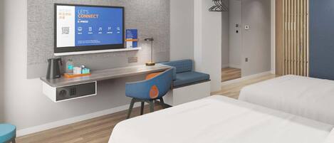 A hotel room with a bed, a desk with a computer, a seating area, and a television displaying a QR code.