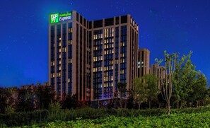 A multi-story hotel with a prominent Holiday Inn Express sign, surrounded by greenery. - Holiday Inn Express Urumqi Station by IHG (Ürümqi)