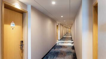 A hotel hallway with a wooden door on the left, a sign with the number 1402, and a long corridor with doors on both sides.