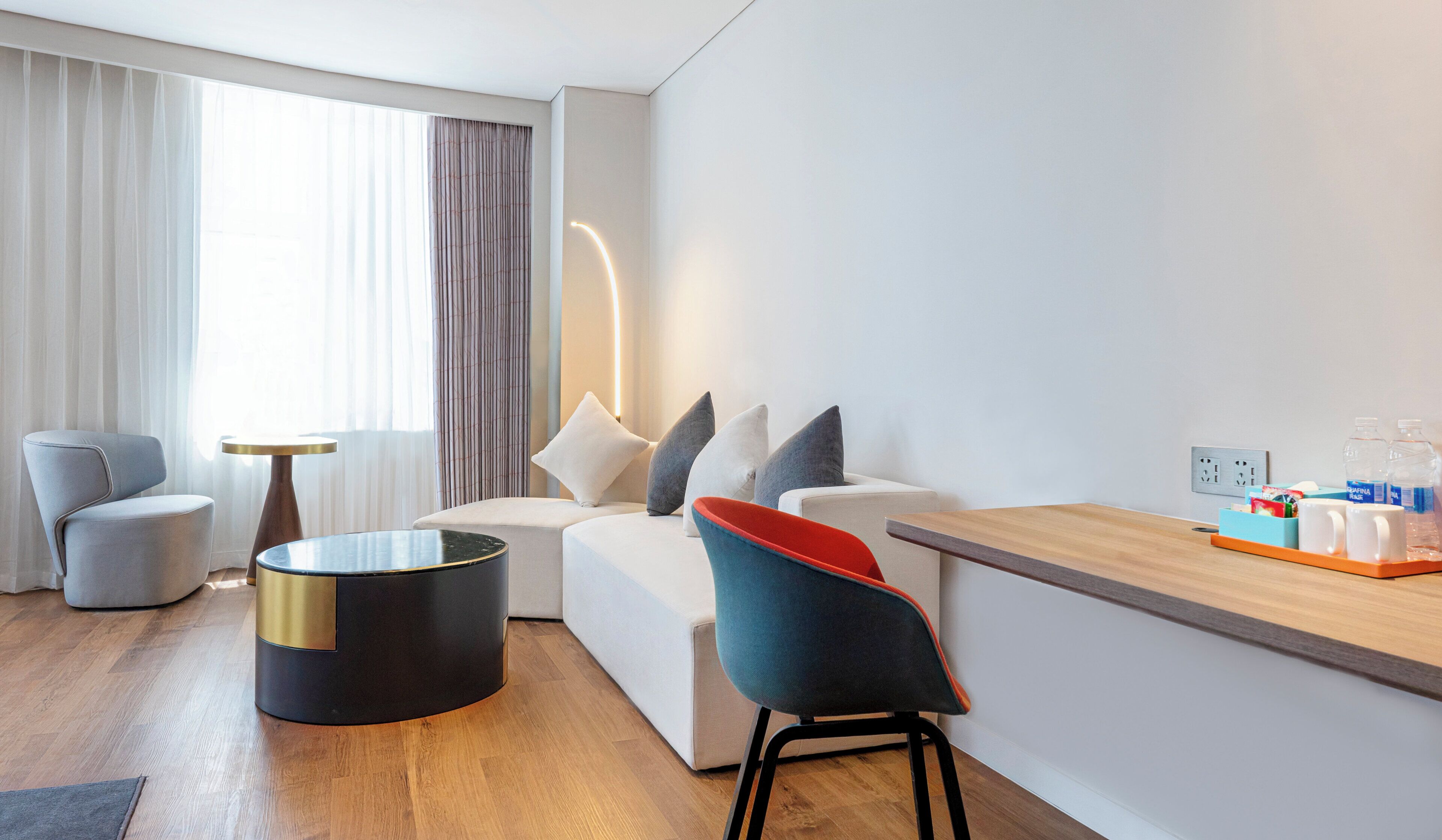 A modern hotel room with a sofa, armchairs, a coffee table, and a small dining table with a tray.