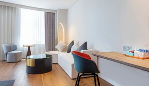 Een moderne hotelkamer met een bank, fauteuils, een salontafel en een eettafeltje met een dienblad.