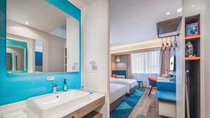 Habitación de hotel con un espejo grande, un lavamanos blanco, una pared de acento azul, una cama con ropa de cama azul, un escritorio pequeño y una silla.