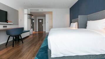 A modern hotel room with a large bed, a desk, and a television.