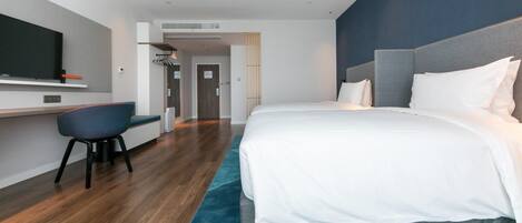 A modern hotel room with a large bed, a desk, and a television.