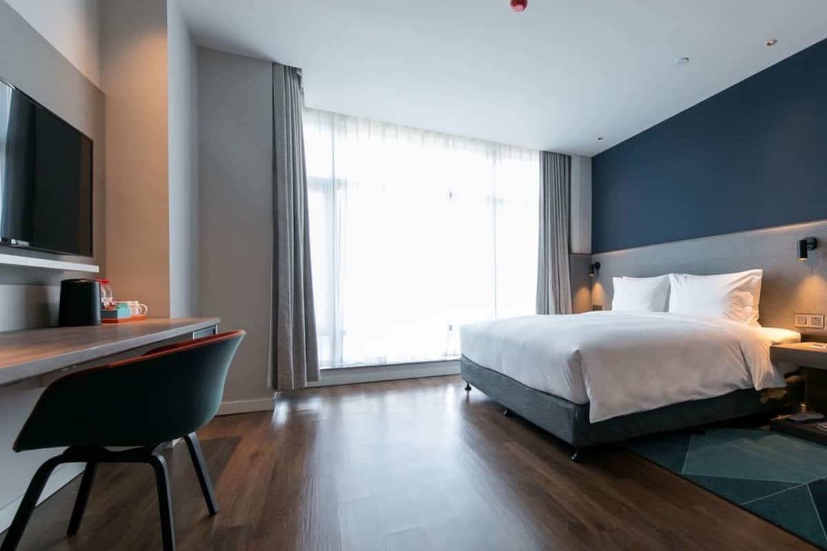 A modern hotel room with a bed, bedside table, desk, chair, and a TV.