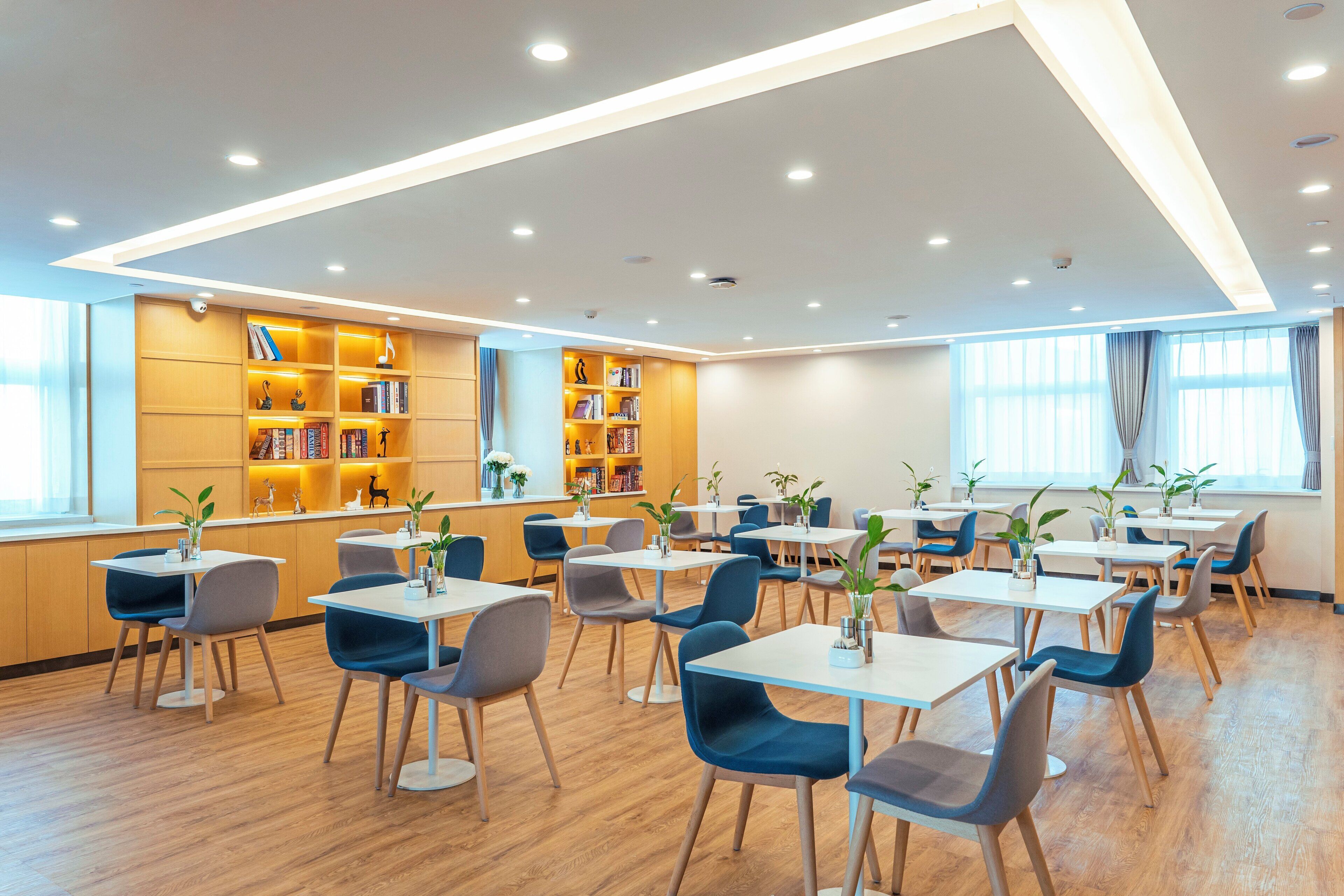 Un comedor moderno con mesas y sillas, una estantería y un amplio ventanal.