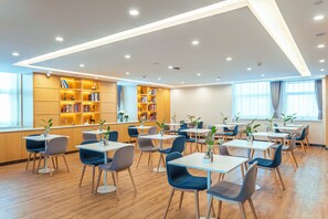 A modern dining area with tables and chairs, a bookshelf, and a large window. - Holiday Inn Express Urumqi Station by IHG (Ürümqi)