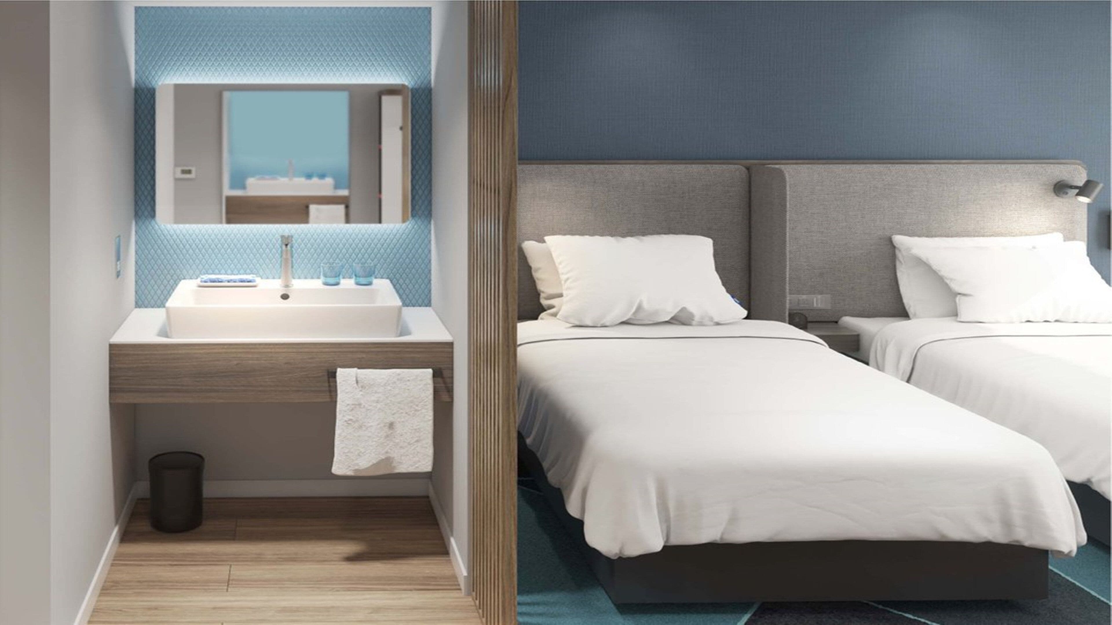 A hotel room with a bathroom, two beds, a mirror, and a view of the city.
