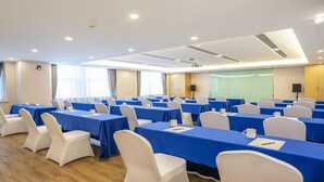 Un salón de conferencias con varias mesas y sillas, equipado con micrófonos y altavoces, y una pantalla grande para presentaciones.