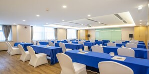 Un salón de conferencias con varias mesas y sillas, equipado con micrófonos y altavoces, y una pantalla grande para presentaciones.