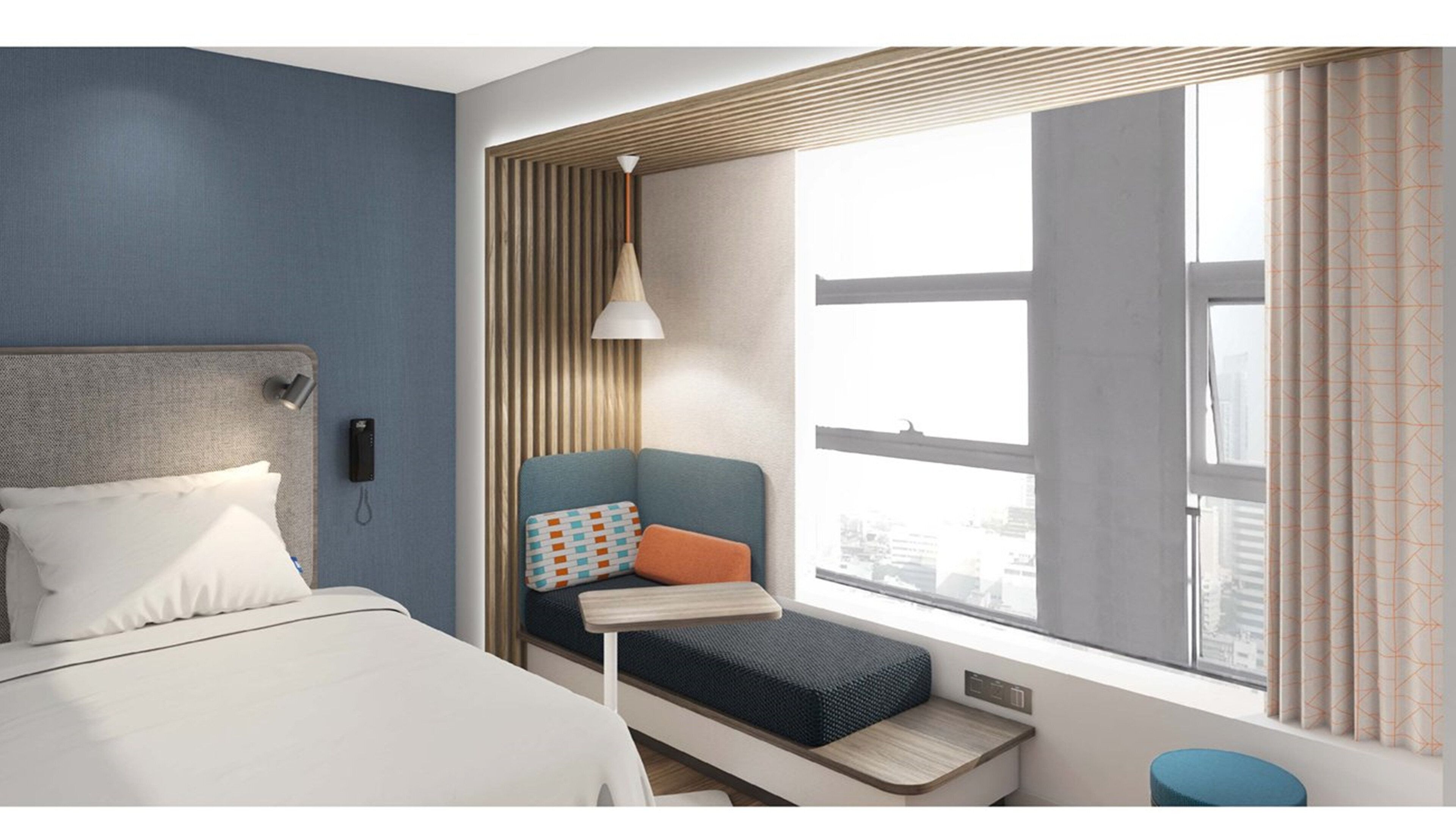 Una habitación de hotel moderna con una cama, un pequeño rincón de descanso con un banco y cojines, un escritorio y un amplio ventanal con cortinas.