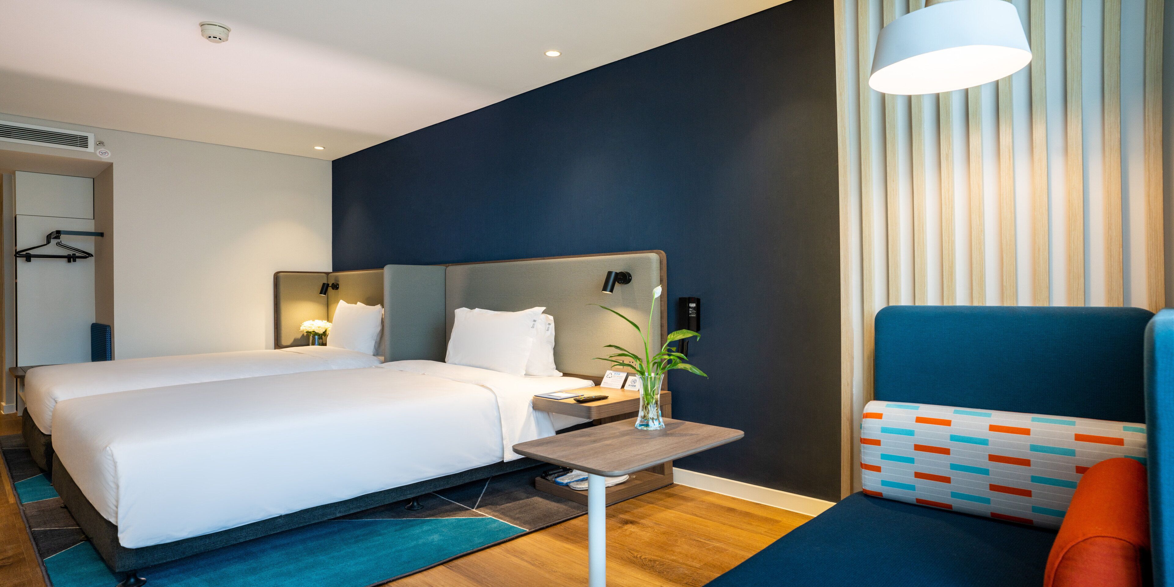 Et hotelværelse med en dobbeltseng, et sengebord med lampe, en stol og udsigt ud.