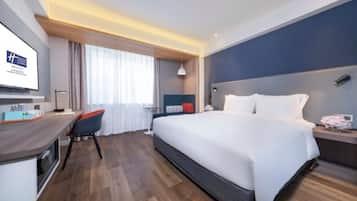 Een moderne hotelkamer met een groot bed, een bureau met stoel, een televisie en een raam met gordijnen.
