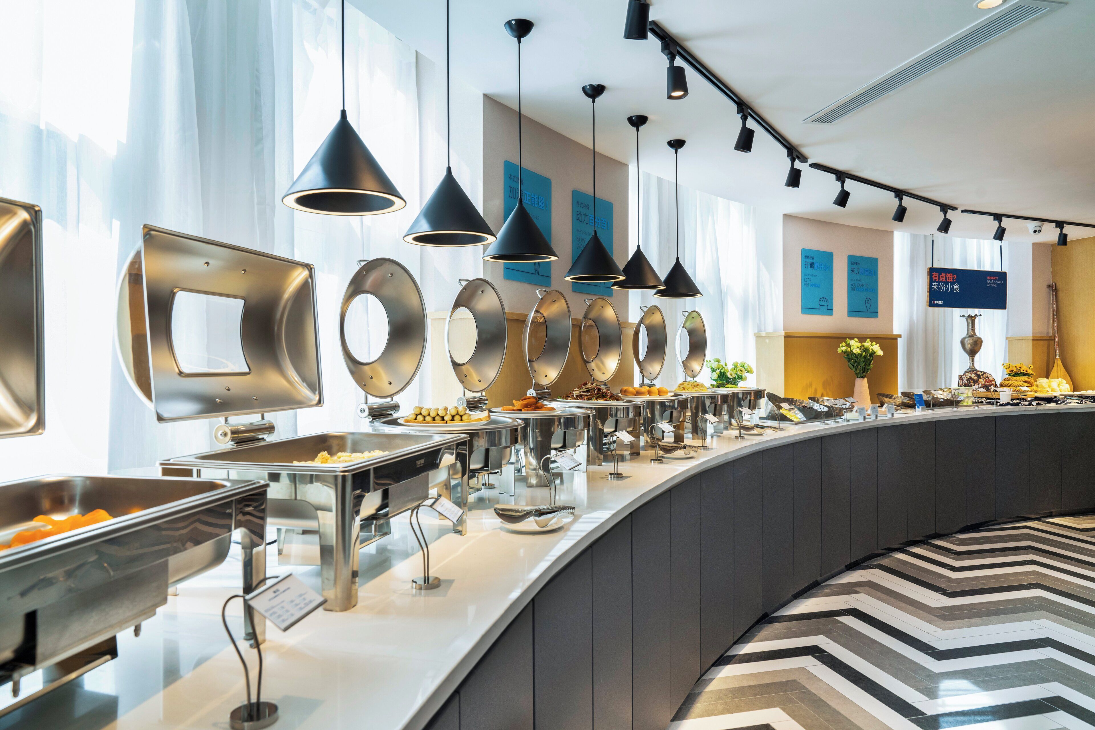 Een buffetgedeelte met verschillende food stations, verlichtingsarmaturen en een modern interieur.