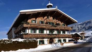 A traditional wooden chalet with a sloped roof, balconies, and a snow-covered landscape.