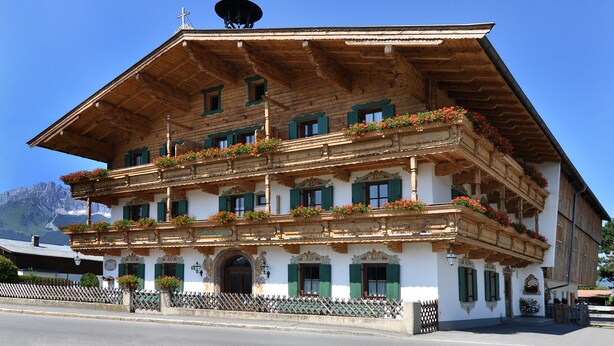 A traditional wooden building with multiple balconies, green shutters, and flower boxes. - Kaiserpension Müllnerhof (Oberndorf in Tirol)