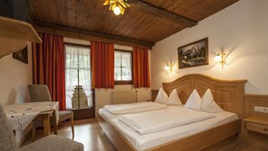 A wooden bed with white linens, a wooden desk, and a chair in a room with wooden floors and a sloped ceiling. - Kaiserpension Müllnerhof (Oberndorf in Tirol)